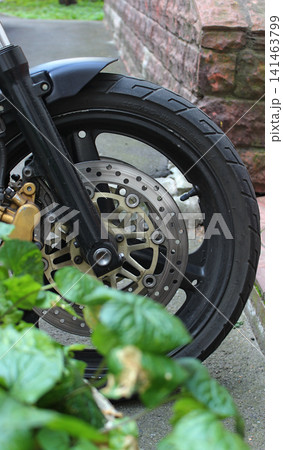 Front Wheel Of Modern Street Motorbike Near City Planter In Front Of Entrance To Residential Building. Motorcycle Parking Vertical Stock Image Front Wheel Of Modern Street Motorbike Near City Planter In Front Of Entrance To Residential Building. Motorcycle Parking Vertical Stock Image 141463799