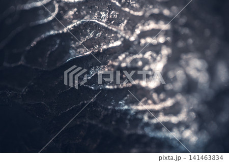 Close-up of textured metallic surface with intricate patterns and reflections, showcasing a blend of light and shadow in a dark setting Close-up of textured metallic surface with intricate patterns and reflections, showcasing a blend of light and shadow in a dark setting 141463834