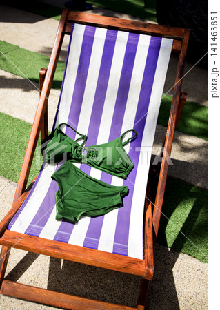 Green bikini set displayed on a purple and white striped lounge chair under sunlight, surrounded by green grass and outdoor elements 141463851