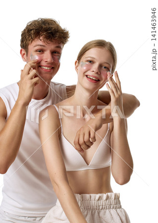 Playful fair-skinned young couple applying facial cream and smiling at camera Playful fair-skinned young couple applying facial cream and smiling at camera 141463946