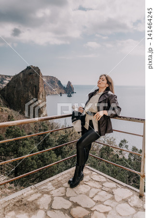 Woman coast travel stylish young lady leaning on a railing at a scenic clifftop overlook by the ocean Woman coast travel stylish young lady leaning on a railing at a scenic clifftop overlook by the ocean 141464245