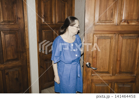 elderly woman in blue dress stands classic wooden door, her posture radiating gentle anticipation welcomes visitor heartfelt scene connection, warmth, and quiet joy reunion familiar homely setting 141464458