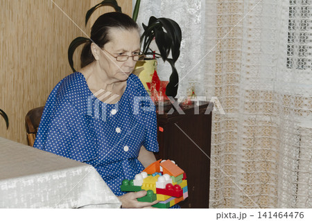 grandmother blue dress shares joyful moment with her grandson build with colorful blocks, their smiles reflecting the warmth family bonding and the simple delight creative play in cozy, familiar room grandmother blue dress shares joyful moment with her grandson build with colorful blocks, their smiles reflecting the warmth family bonding and the simple delight creative play in cozy, familiar room 141464476