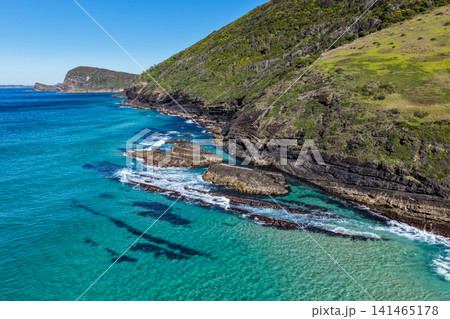 Aerial view of the clear turquoise waters surrounding Blueys Head at Blueys Beach, with the rocky headland, pristine sandy shoreline and vibrant coastal waters along the Mid North Coast of NSW. Aerial view of the clear turquoise waters surrounding Blueys Head at Blueys Beach, with the rocky headland, pristine sandy shoreline and vibrant coastal waters along the Mid North Coast of NSW. 141465178