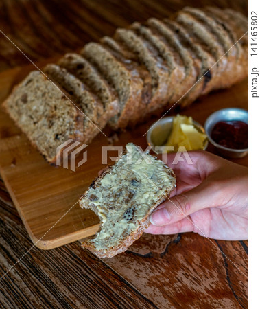Hand Holding Buttered Whole Wheat Bread Slice with Artisan Loaf on Wooden Cutting Board, Rustic Homemade Breakfast and Bakery Lifestyle Concept Hand Holding Buttered Whole Wheat Bread Slice with Artisan Loaf on Wooden Cutting Board, Rustic Homemade Breakfast and Bakery Lifestyle Concept 141465802