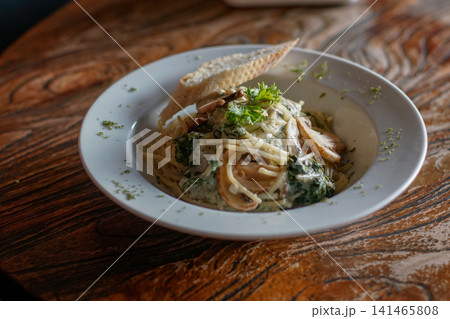 Creamy Mushroom Spaghetti with Spinach and Garlic Bread Served in White Bowl, Italian Restaurant Pasta Dish and Comfort Food on Rustic Wooden Table Creamy Mushroom Spaghetti with Spinach and Garlic Bread Served in White Bowl, Italian Restaurant Pasta Dish and Comfort Food on Rustic Wooden Table 141465808
