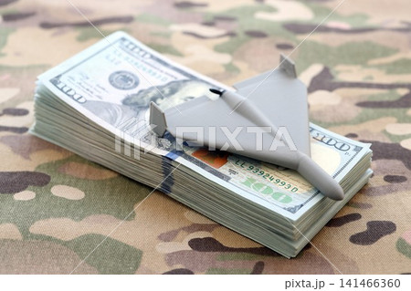 Unnamed grey toy drone and dollar bills on camouflage fabric. Drone manufacturing funds Unnamed grey toy drone and dollar bills on camouflage fabric. Drone manufacturing funds 141466360