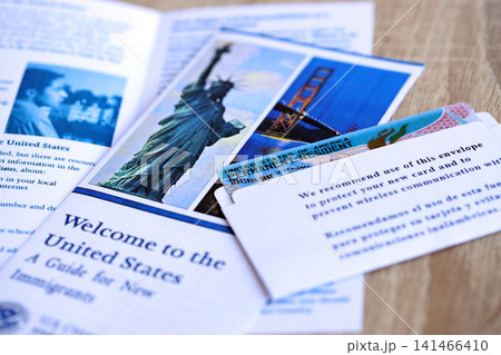 Permanent resident green card in envelope and guide for new immigrants lies on wooden table 141466410