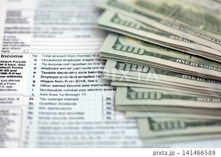 Big amount of United States hundred dollar bills in bunch on table with tax return form Big amount of United States hundred dollar bills in bunch on table with tax return form 141466589