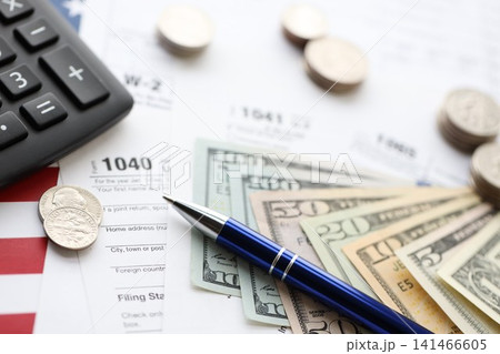 American US dollars money bills and coins with pen and calculator on IRS tax form blanks American US dollars money bills and coins with pen and calculator on IRS tax form blanks 141466605