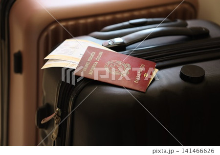 Italian passport with tickets lies on touristic suitcase close up in airport waiting hall Italian passport with tickets lies on touristic suitcase close up in airport waiting hall 141466626