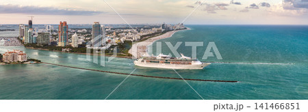 Luxurious cruise ocean liner sailing at Miami port harbor through main channel near South Beach. Hotels and residential buildings on waterfront and high skyscraper towers of downtown in distance 141466851