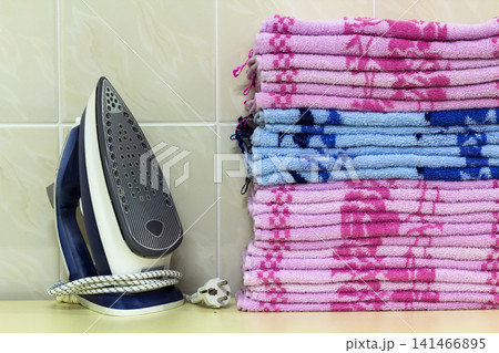 Ironing linen with steam generator. A stack of ironed towels lying next to the iron. Teflon sole plate covered with small holes. Ironing linen with steam generator. A stack of ironed towels lying next to the iron. Teflon sole plate covered with small holes. 141466895