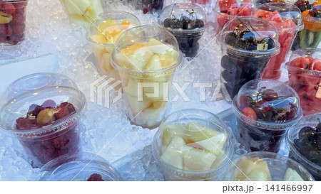 Fresh sliced fruits and berries in plastic cups displayed on crushed ice Fresh sliced fruits and berries in plastic cups displayed on crushed ice 141466997