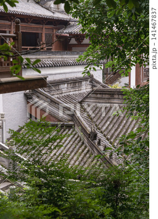 High-angle shot capturing the sweeping tiled roofs, carved wooden eaves, and stone courtyards of an ancient temple nestled within the Dazu Rock Carvings complex. High-angle shot capturing the sweeping tiled roofs, carved wooden eaves, and stone courtyards of an ancient temple nestled within the Dazu Rock Carvings complex. 141467837