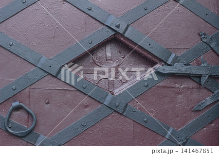 Medieval style black iron strap hinge on old painted wooden door close up Medieval style black iron strap hinge on old painted wooden door close up 141467851