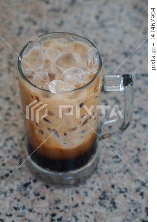 top view Iced black coffee with milk, served in a large handled glass mug and placed on a marble surface background, cool, food, drink, sweet, copy space top view Iced black coffee with milk, served in a large handled glass mug and placed on a marble surface background, cool, food, drink, sweet, copy space 141467904