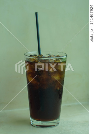 front view closeup cool and fresh dark-colored drink with ice, black tube in a clear glass, placed on a concrete surface background, food, drink, object, decor, decoration, copy space 141467924