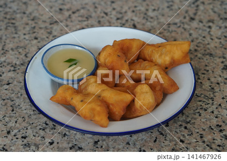 hot four pieces of patongko and condensed milk in a ceramic cup, placed on a white and blue enamel plate on a marble surface background, food, dessert, copy space 141467926