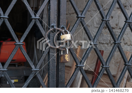 Two padlocks securing a black wrought iron lattice gate close up Two padlocks securing a black wrought iron lattice gate close up 141468270