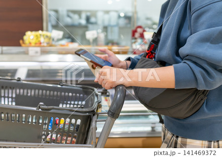 ショッピングカートを押して食品売り場を回る女性のクローズアップ ショッピングカートを押して食品売り場を回る女性のクローズアップ 141469372