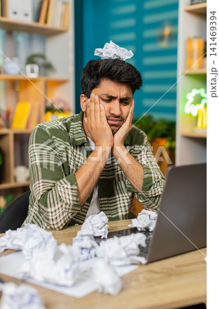 Indian man on home table feeling frustrated with crumpled paper near laptop during hard remote work 141469394