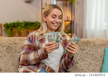 Woman counting cash money at home, smiling proudly while planning budget after lottery win or raise 141469433
