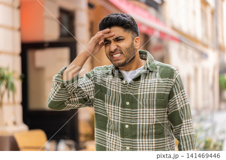Indian man having strong headache walking in city street touching forehead with painful expression Indian man having strong headache walking in city street touching forehead with painful expression 141469446