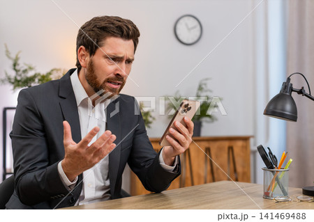 Middle-aged businessman frustrated reading client rejection on smartphone frowns at news loses game Middle-aged businessman frustrated reading client rejection on smartphone frowns at news loses game 141469488