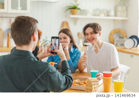 Cheers Funky mood. Happy group of friends posing for mobile photo. Man taking photo of friends at party. Group of multiracial young people taking photo on phone. Young people enjoy their company smile Cheers Funky mood. Happy group of friends posing for mobile photo. Man taking photo of friends at party. Group of multiracial young people taking photo on phone. Young people enjoy their company smile 141469634