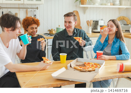 Home party. Friends spending time together having fun laughing communicating at home. Happy diverse group eating pizza drinking beer or lemonade. Mixed race young buddies best friends enjoying weekend 141469716