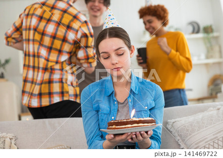 Sad lonely frustrated unhappy young woman looking at birthday cake with candle on birthday party. Girl sad disappointed thinking about life. Birthday party with friends. People celebrating birthday 141469722