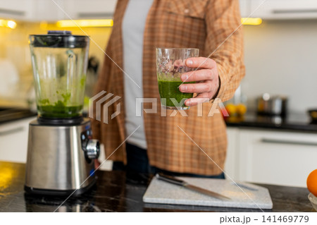 Unrecognizable man pouring green smoothie from blender in kitchen for healthy detox nutrition 141469779
