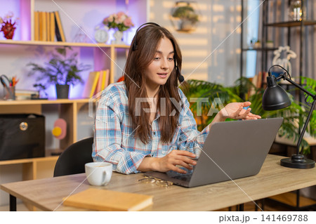 Young woman on home table using headset laptop for calm customer support video call in living room Young woman on home table using headset laptop for calm customer support video call in living room 141469788