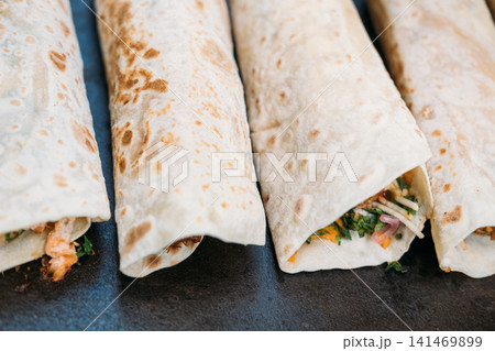 Tortilla roll. Burrito set. Traditional fast meal with spicy vegetable prepared on black background. Grilled pita dinner snack dish. 141469899