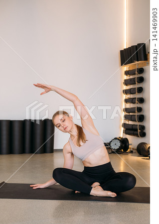 Stretching side. Yoga exercise. Female in sportswear bending torso sideways leaning in sitting lotus pose for spine muscle recreation. Stretching side. Yoga exercise. Female in sportswear bending torso sideways leaning in sitting lotus pose for spine muscle recreation. 141469903
