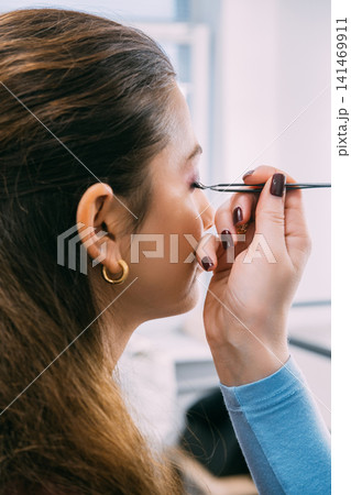 Applying false eyelashes. Female beauty. Beautician expert using tweezers for cosmetic treatment extension procedure. Applying false eyelashes. Female beauty. Beautician expert using tweezers for cosmetic treatment extension procedure. 141469911