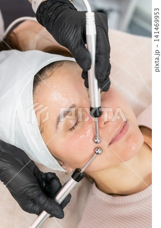 Microcurrent skincare. Female procedure. Esthetician hands in black gloves using professional modern device for lifting client face in salon. 141469953