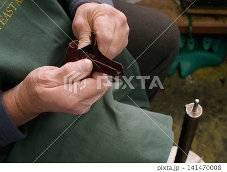 Professional shoemaker. Fixing footwear. Unrecognizable skilled cobbler hands with leather heel for manufacturing in workshop. 141470008