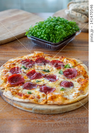Freshly baked homemade pepperoni pizza with melted cheese and herbs served on a rustic wooden board. Artisan Italian cuisine, comfort food, restaurant menu, and recipe concept. Freshly baked homemade pepperoni pizza with melted cheese and herbs served on a rustic wooden board. Artisan Italian cuisine, comfort food, restaurant menu, and recipe concept. 141470546