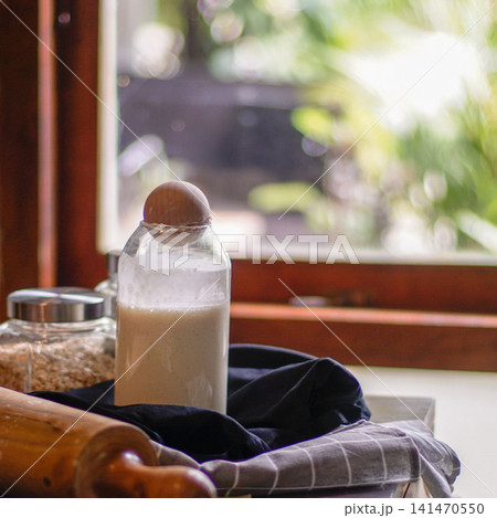 Rustic Sourdough Starter by Sunny Kitchen Window with Baking Tools and Grains, Artisan Homemade Bread Fermentation 141470550