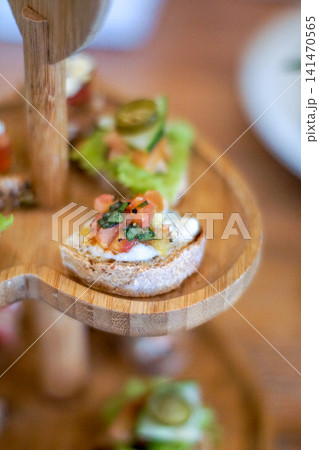 Close Up Gourmet Canape with Fresh Tomato Herbs and Cheese on Artisan Bread Served on Rustic Wooden Tiered Stand Elegant Finger Food Appetizer for Cafe Catering and Fine Dining 141470565