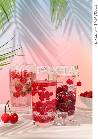Modern still life with berry juice, raspberries, cherries, red currants, and ice on an elegant kitchen table, casting long, sharp shadows. The concept is a minimal detox diet, summer vitamin drinks 141470611