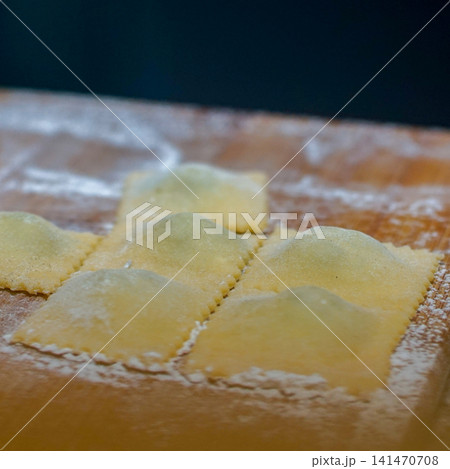 Fresh Handmade Ravioli on Floured Wooden Board, Traditional Italian Fresh Pasta Preparation, Artisan Homemade Cuisine, Rustic Cooking Process and Fresh Dough Concept Fresh Handmade Ravioli on Floured Wooden Board, Traditional Italian Fresh Pasta Preparation, Artisan Homemade Cuisine, Rustic Cooking Process and Fresh Dough Concept 141470708