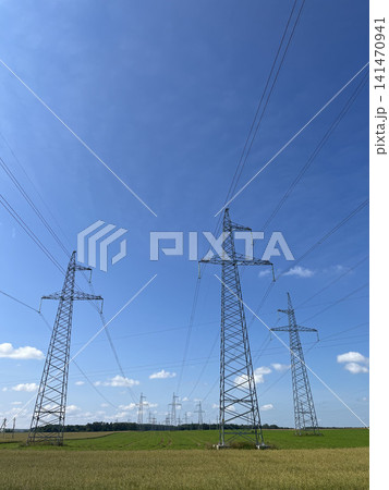 High voltage electricity transmission towers with power lines across rural green farmland landscape 141470941