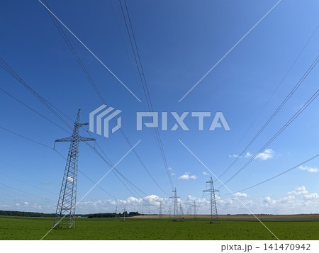 High voltage electricity transmission towers with power lines across green fields under blue sky 141470942