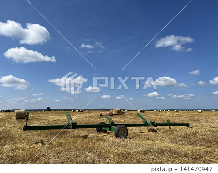 Green header trailer on harvested farmland with hay bales beneath a bright summer sky landscape Green header trailer on harvested farmland with hay bales beneath a bright summer sky landscape 141470947