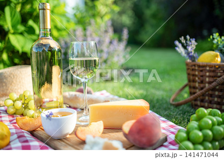 Summer picnic with white wine cheese peaches honey and grapes in green backyard garden 141471044