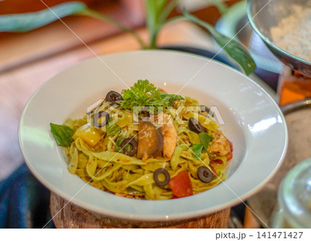 Pasta with Salmon, Black Olives, Colorful Vegetables and Fresh Herbs Served in a White Bowl at a Restaurant 141471427