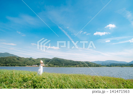 青空の下で湖畔の草原に立つ女性 141471563